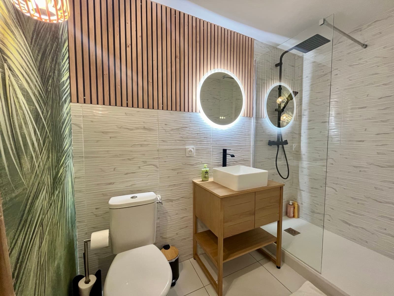 Salle de bain au papier peint tropical avec toilette et vasque sur meuble bois